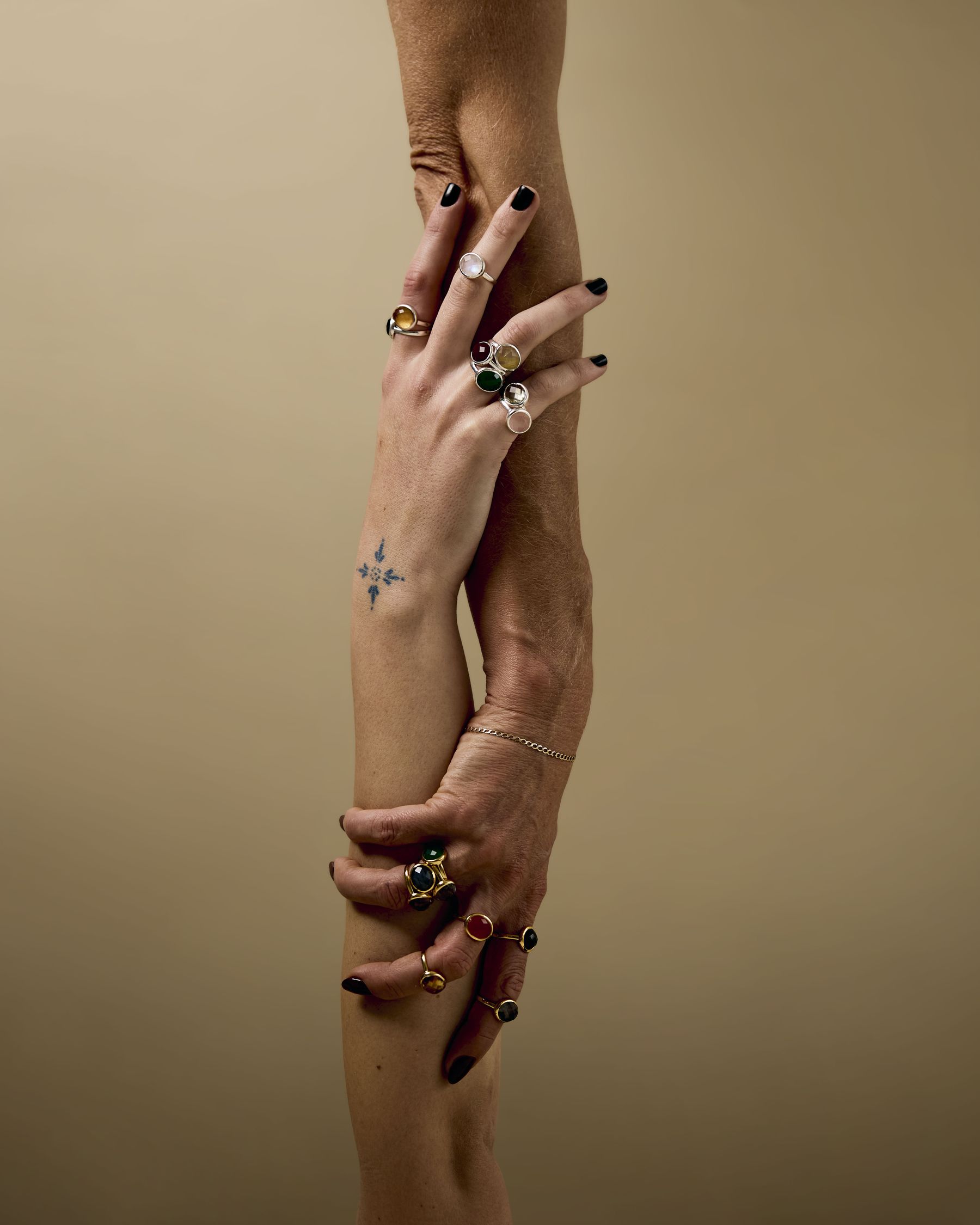 Two forearms intertwined, stacked with gold and stone rings
