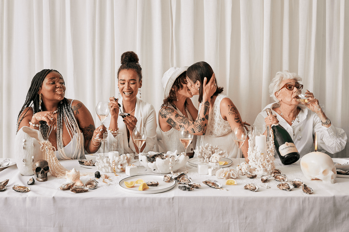 Women laughing around a long table set with pearls, shells and champagne