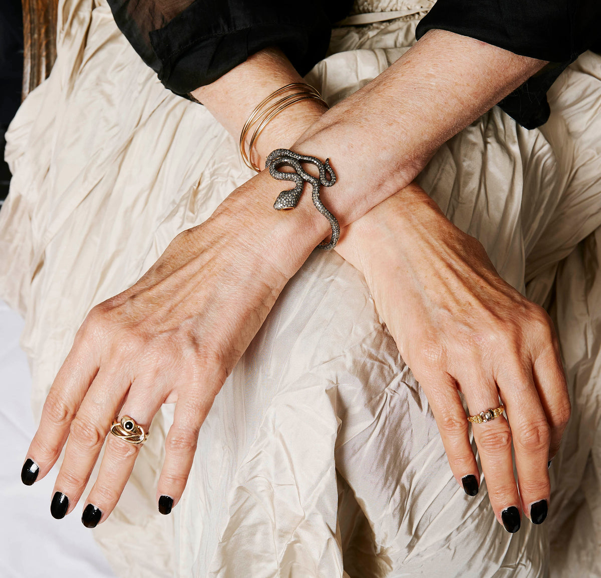 Hands wearing a diamond snake bangle and gemstone rings
