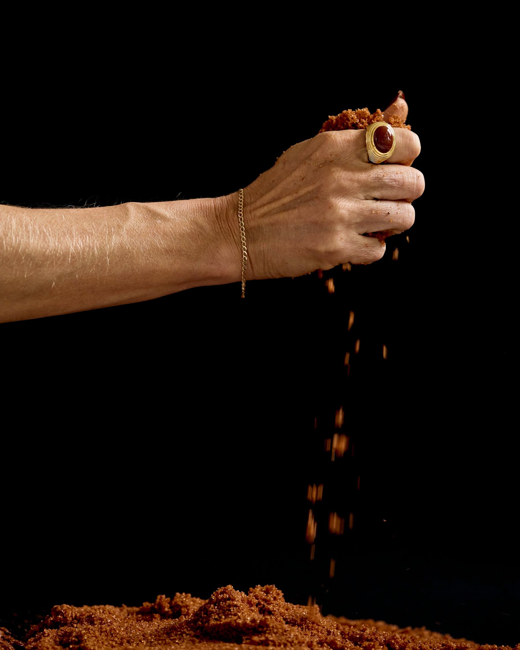 A ringed hand letting red earth fall through its fingers