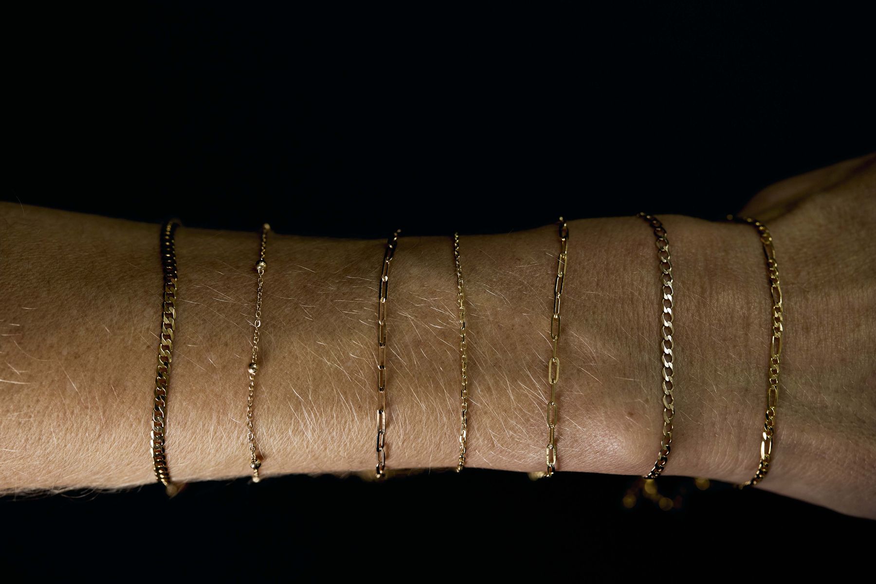 A wrist stacked with fine gold chains, lit against black